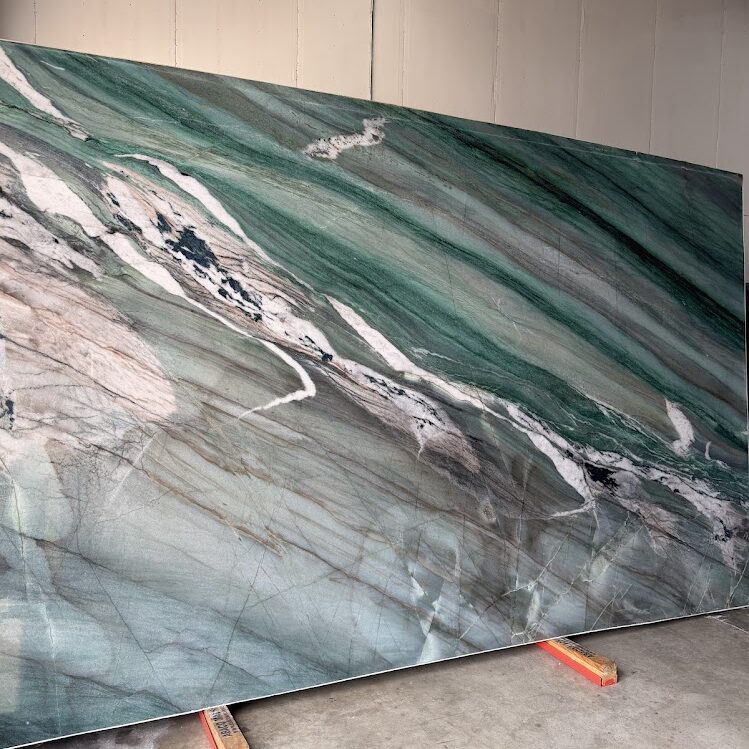 A large-format Brazilian natural stone slab, Mocamblu, displaying a dramatic wave of deep greens, rich earth tones, and striking white mineral veins.