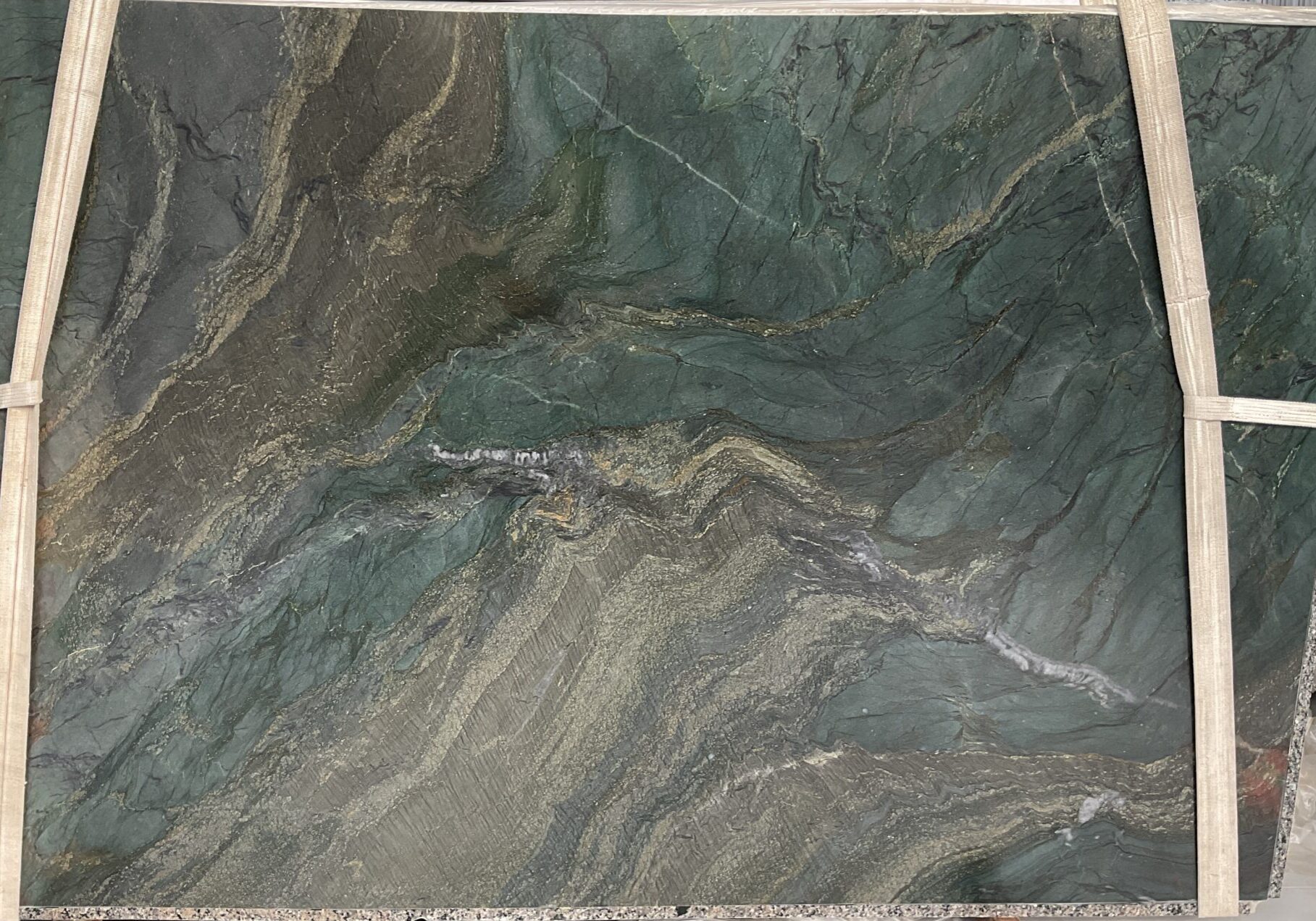 A large-format view of a Sombori Crystal quartzite slab showcasing its rich green tones, sweeping bronze waves, and shimmering crystal quartz movement.