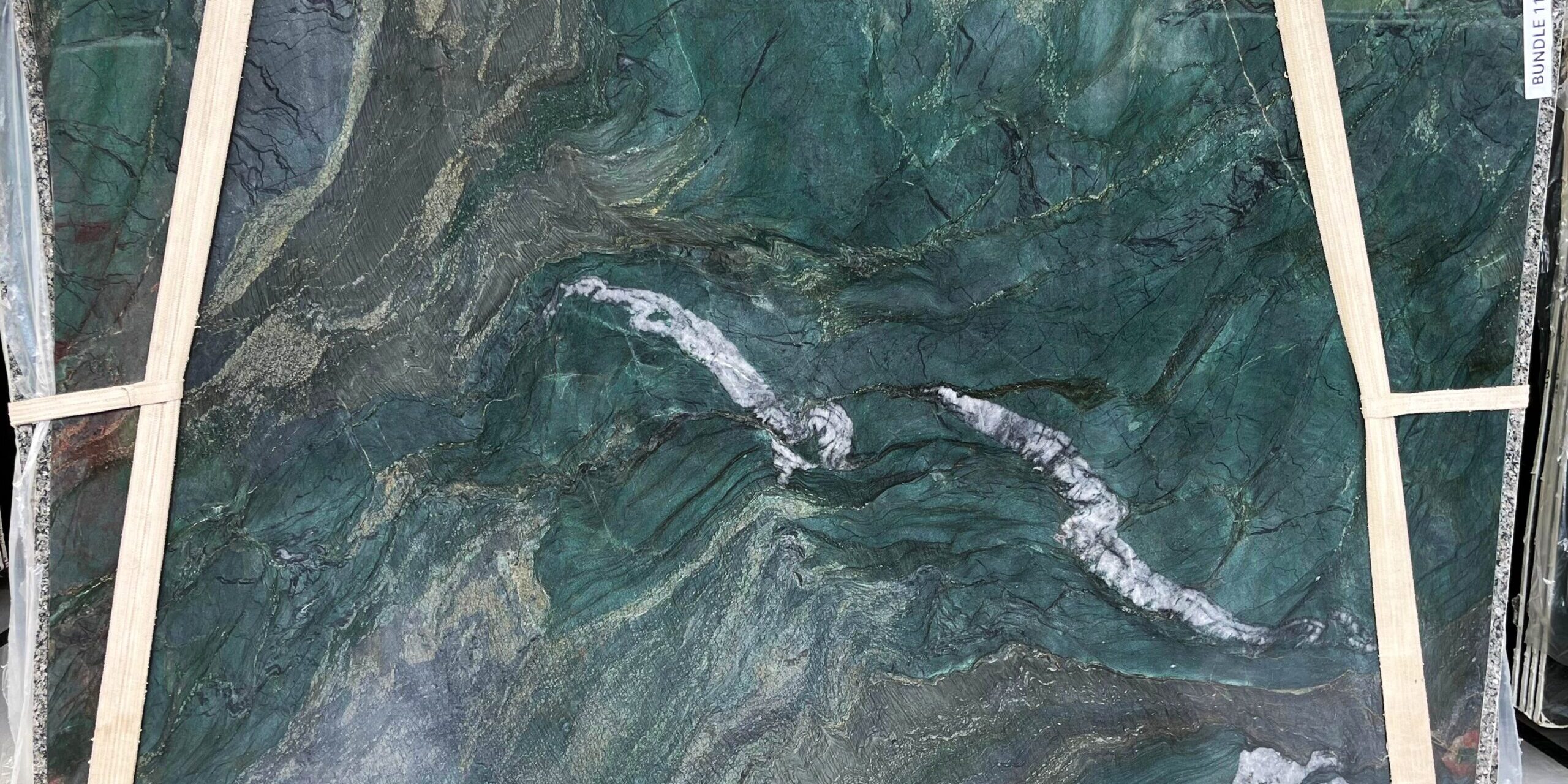 Large format green natural stone slab showcasing high-contrast white veining for architectural projects.