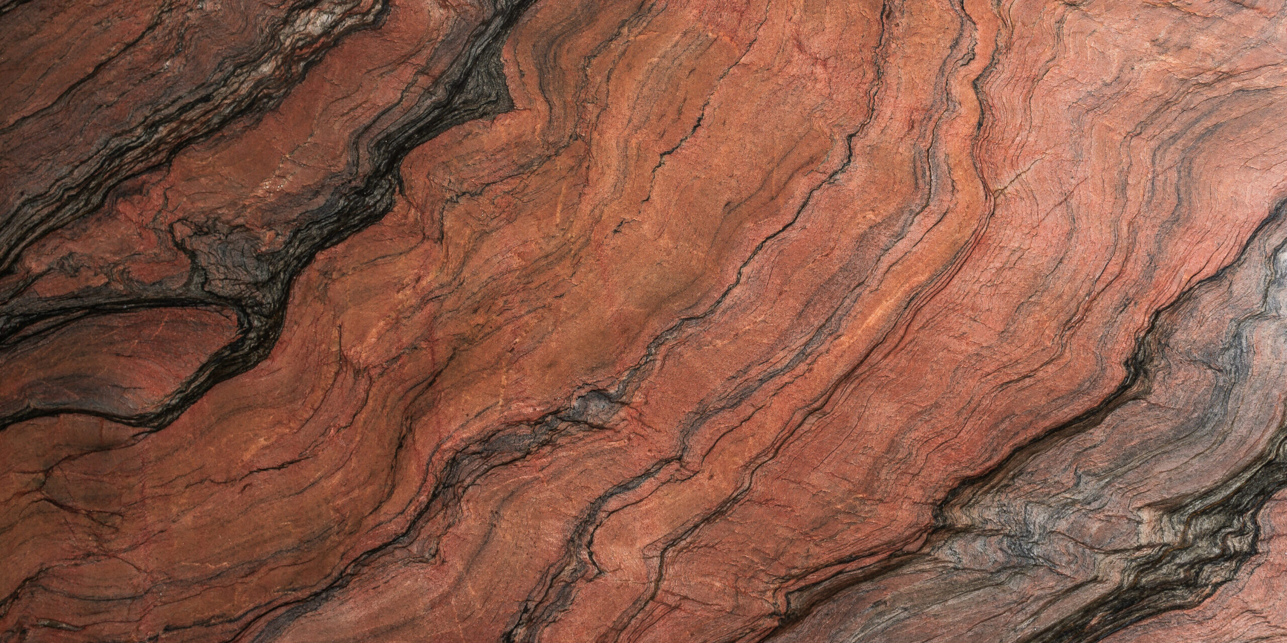 Macro view of red quartzite surface showing intricate terracotta ripples and white quartz crystals.