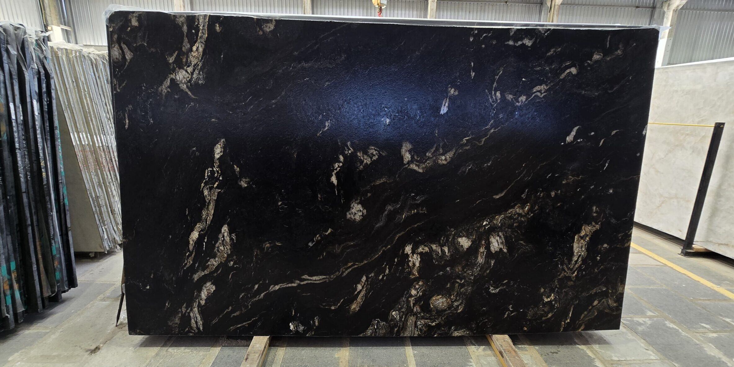 Full portrait of an exotic dark stone slab inside a stone yard, showcasing its rich, flowing gold and copper topography.