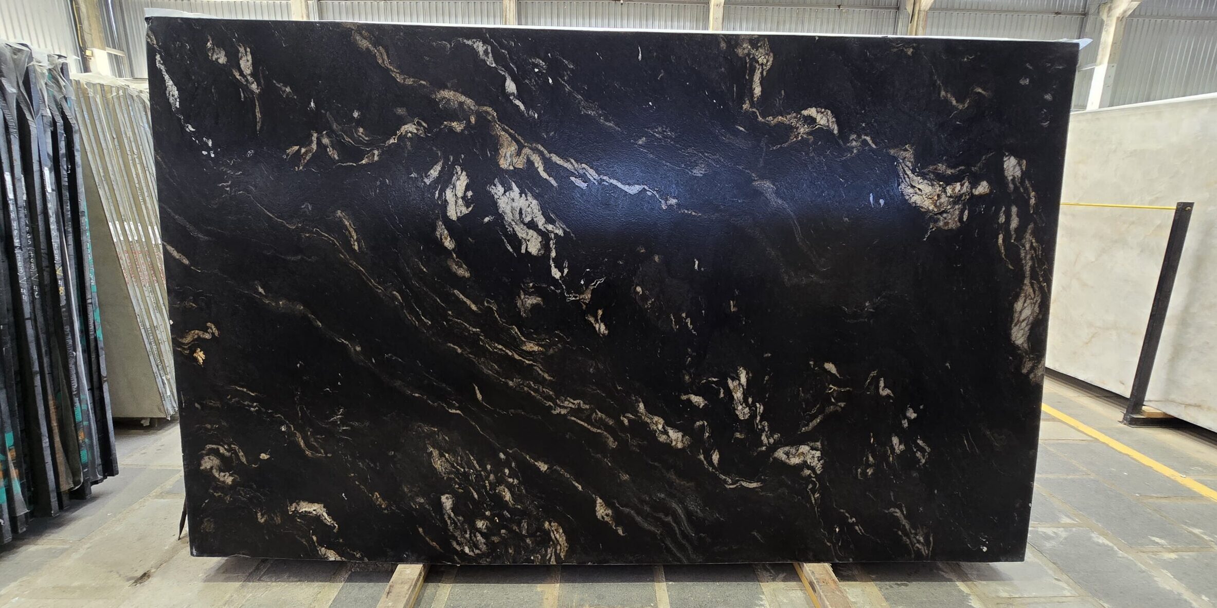 A large-format premium black and gold natural stone slab displaying dense, wavy mineral currents and white quartz streams.