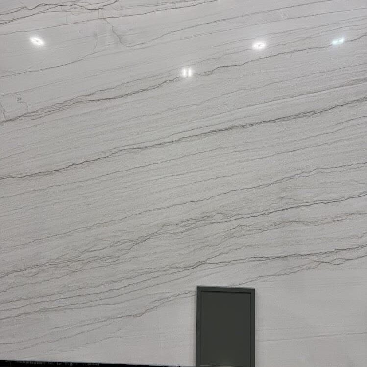 Close-up of the light-reflective surface of a white quartzite slab, positioned next to a dark contemporary cabinet mockup.